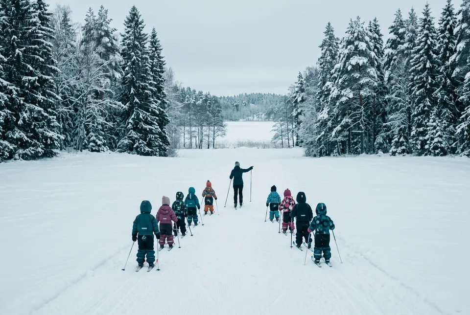 Lapsiryhmä harjoittelee hiihtoa ohjaajan johdolla lumisella aukealla.